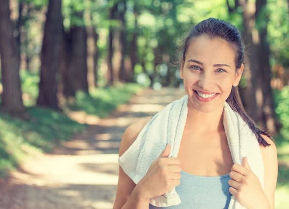 Portrait young attractive smiling fit woman with white towel resting after workout sport exercises outdoors on a background of park trees