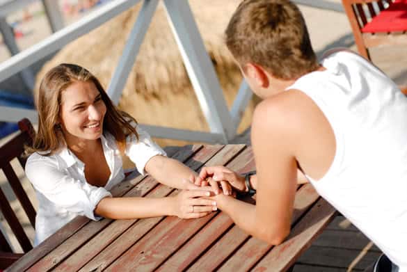 Young beautiful happy romantic couple man and woman holding hands and sitting outdoors on cafe terrace by the sea