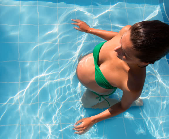 Beautiful pregnant woman sun tanning relaxed at blue pool with green bikini