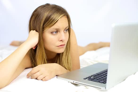 Sad woman looking computer laying in bed