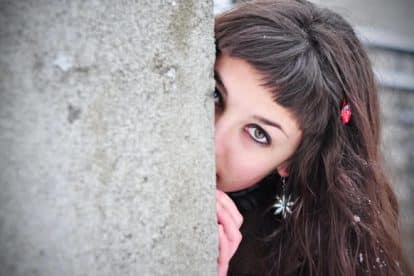 Shy woman hiding behind wall