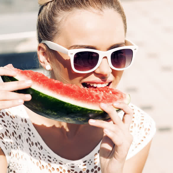 blonde girl with bow tie hair in white summer dress wearing sunglasses bites juicy watermelon