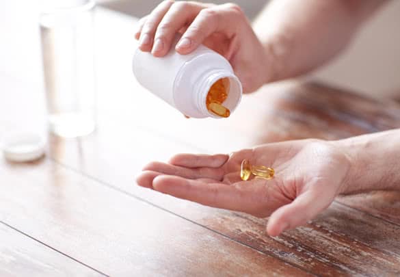 close up of man with glass of water pouring fish oil capsules from jar to hand