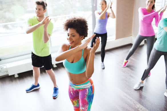 group of smiling people with coach dancing zumba in gym or studio