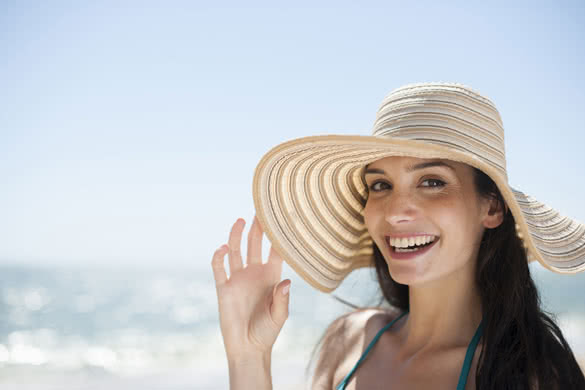 portrait of a beautiful young woman in a swimsuit on the beach protecting herself from the sun with a big hat