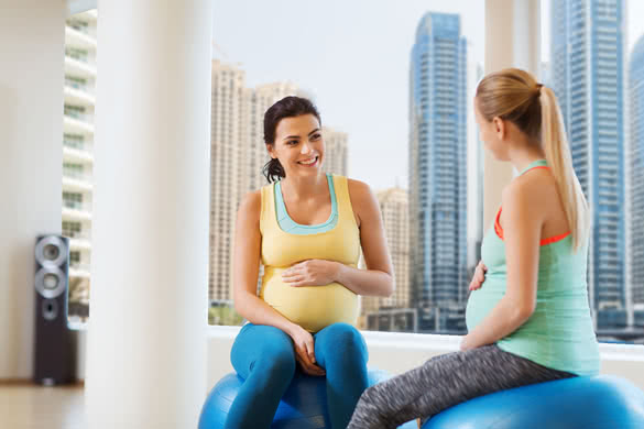 two happy pregnant women sitting and talking on balls in gym