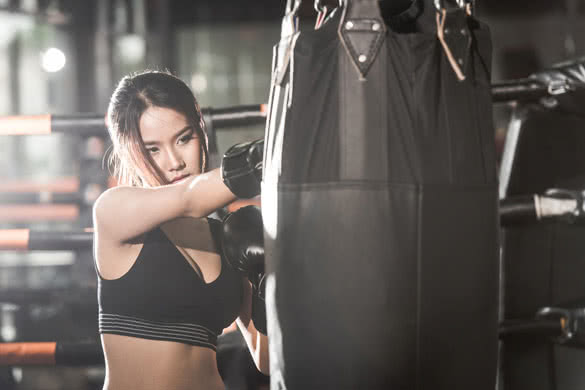 Beautiful Female Punching A Boxing bag With Boxing Gloves at the gym