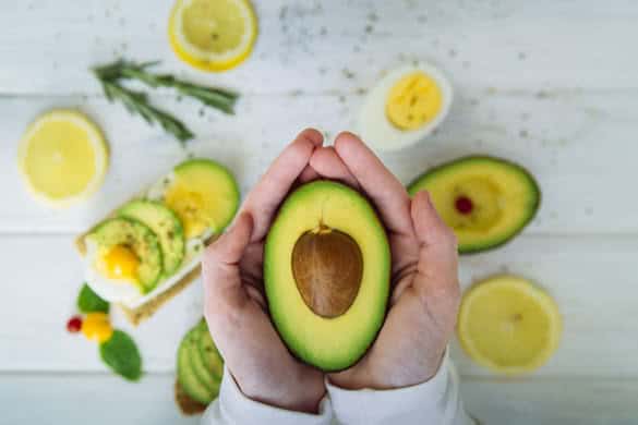 Closeup on hands holding fresh avocado cut in half on light background