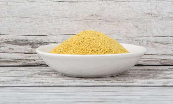 Dried bakers yeast in white bowl over wooden background