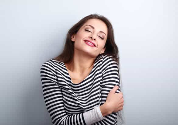 Happy young casual woman hugging herself with natural emotional enjoying face