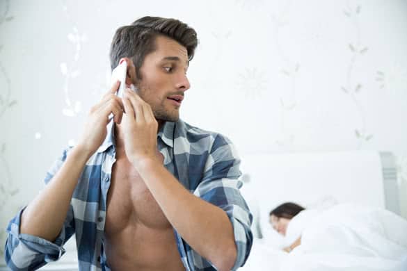 Portrait of a handsome man talking on the phone while his wife sleeping in the bed at home