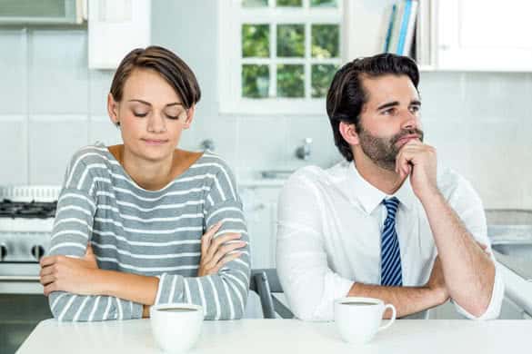 Unhappy couple with coffee cup sitting at table in kitchen