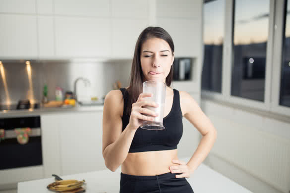 Woman in sportswear drinking sweet banana chocolate protein powder milkshake smoothie