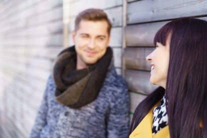 cute woman standing outside looking at her boyfriend in background with a warm smile