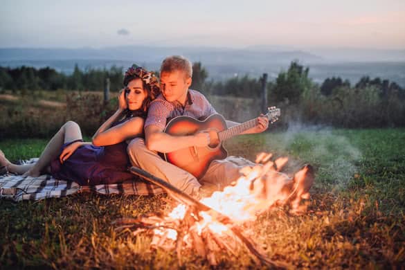 Happy young couple sitting by bonfire with guitar