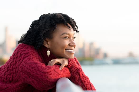 Close up portrait of a young happy african woman leaning on the banister of a bridge near river