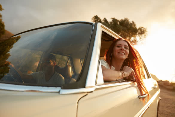 Portrait of happy young woman going on a road trip leaning out of window