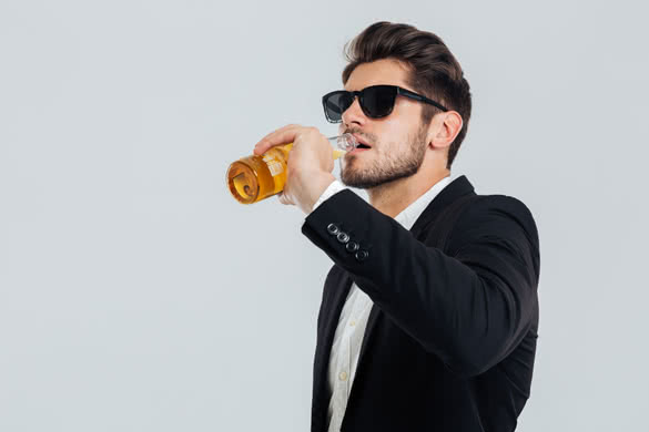 Stylish handsome man in sunglasses and black suit drinking from beer bottle