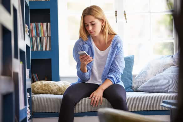 Woman Sitting On Couch At Home Using Mobile Phone