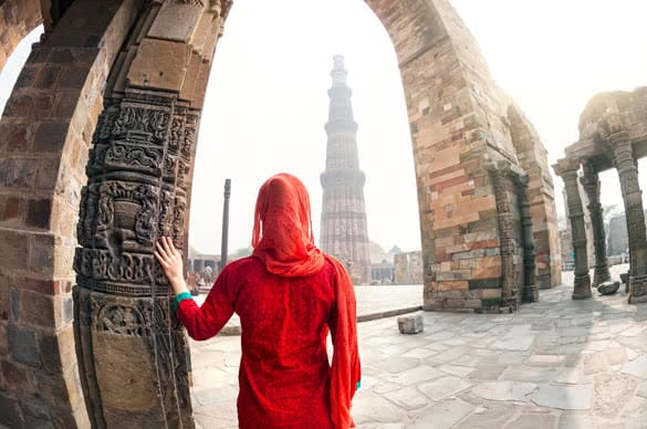 Woman in red costume looking at Qutub Minar tower in Delhi