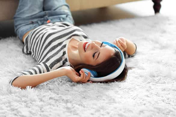 Woman listening music in headphones on carpet in room