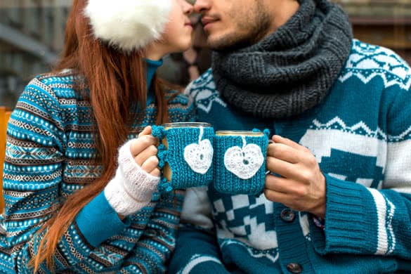 Couple holding knitted coffee cups dressed in sweater