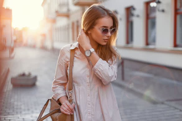 Young beautiful girl in stylish sunglasses and with a fashionable bag at sunset