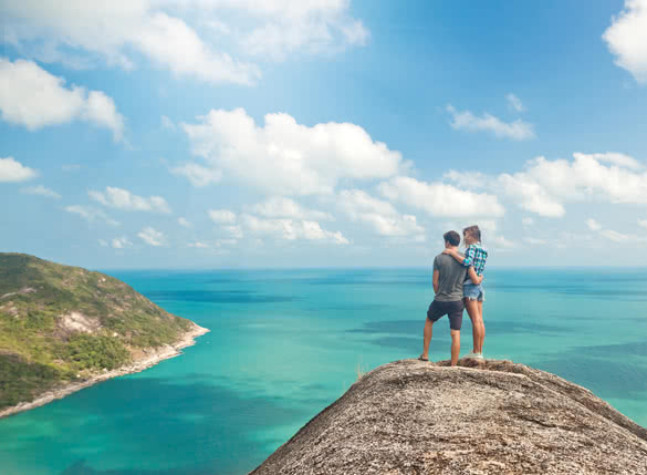 Young couple of travelers on a hill with stunning views of the ocean