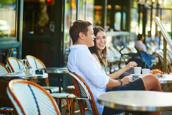 Young romantic couple drinking coffee and eating traditional French croissants in a cozy outdoor cafe in Paris