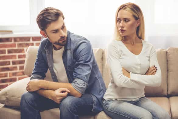 Beautiful couple is sitting back to back on the couch and looking offended at each other while having a quarrel