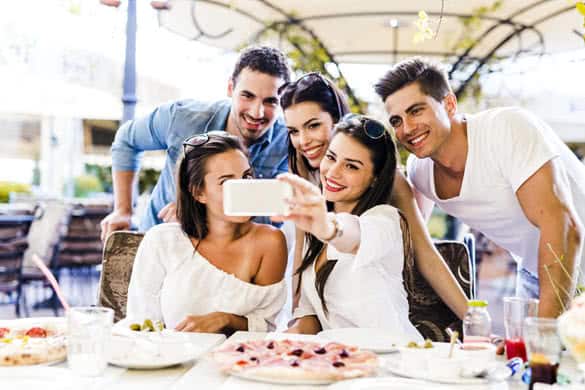 Group of young beautiful people sitting in a restaurant and taking a selfie while smiling