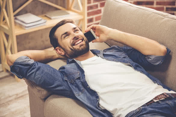 Handsome man in jean clothes is talking on the mobile phone and smiling while lying on couch