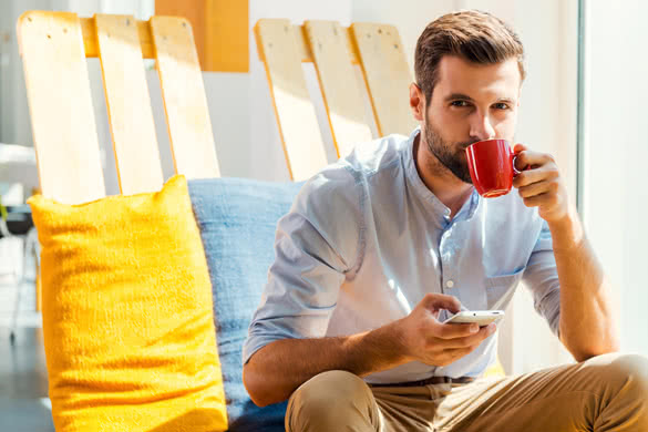 Handsome young man holding mobile phone and drinking coffee while sitting in the rest area of the office 2