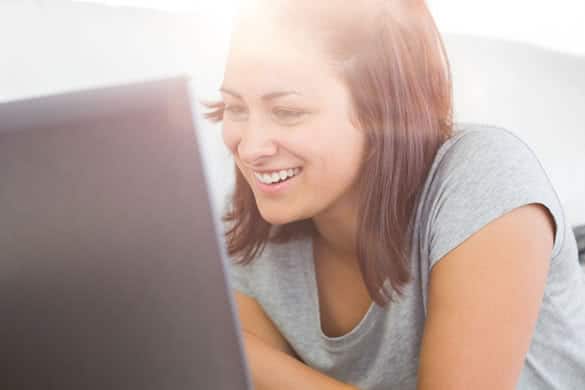 Joyful casual woman working with her notebook while lying on a a couch at home