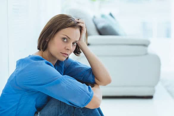 Portrait of sad young woman sitting by sofa at home