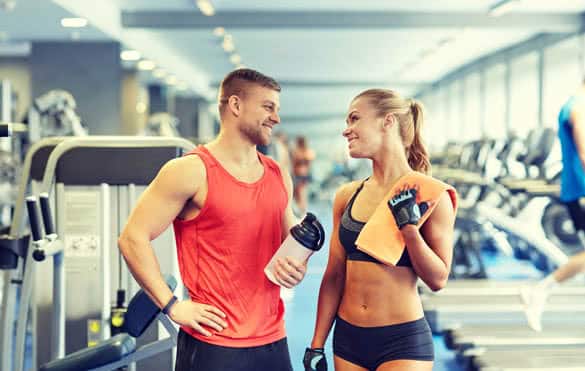 smiling man and woman with protein shake bottle and towel talking in gym