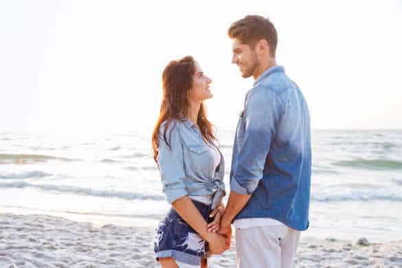 Happy young couple standing and holding hands on the beach