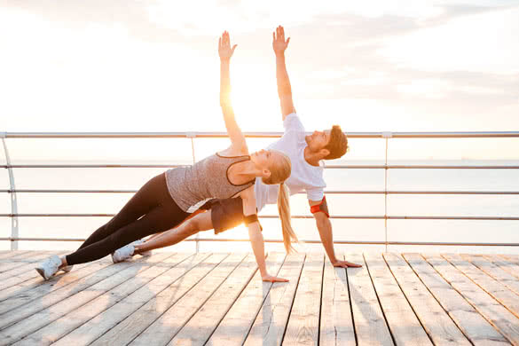 Smiling couple doing yoga exercises outdoors at the beach pier