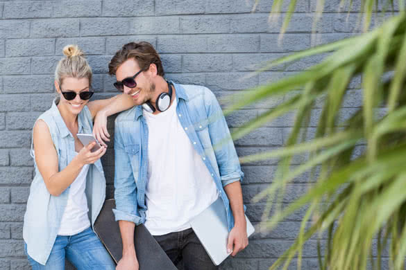 Young couple leaning against wall using mobile phone