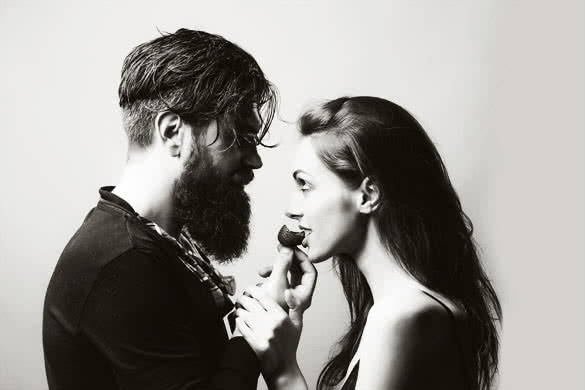 young sexy couple of woman with pretty face and brunette hair with bare shoulders and handsome bearded man with long beard eating red strawberry berry fruit